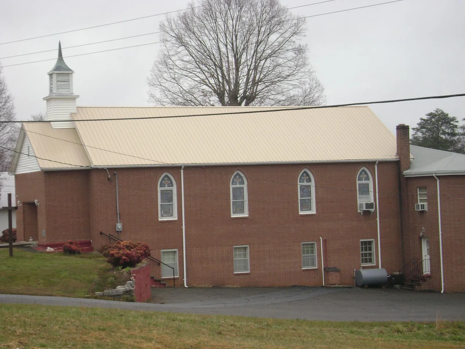 New tan metal roof on a brick church with a white steeple in Homestead